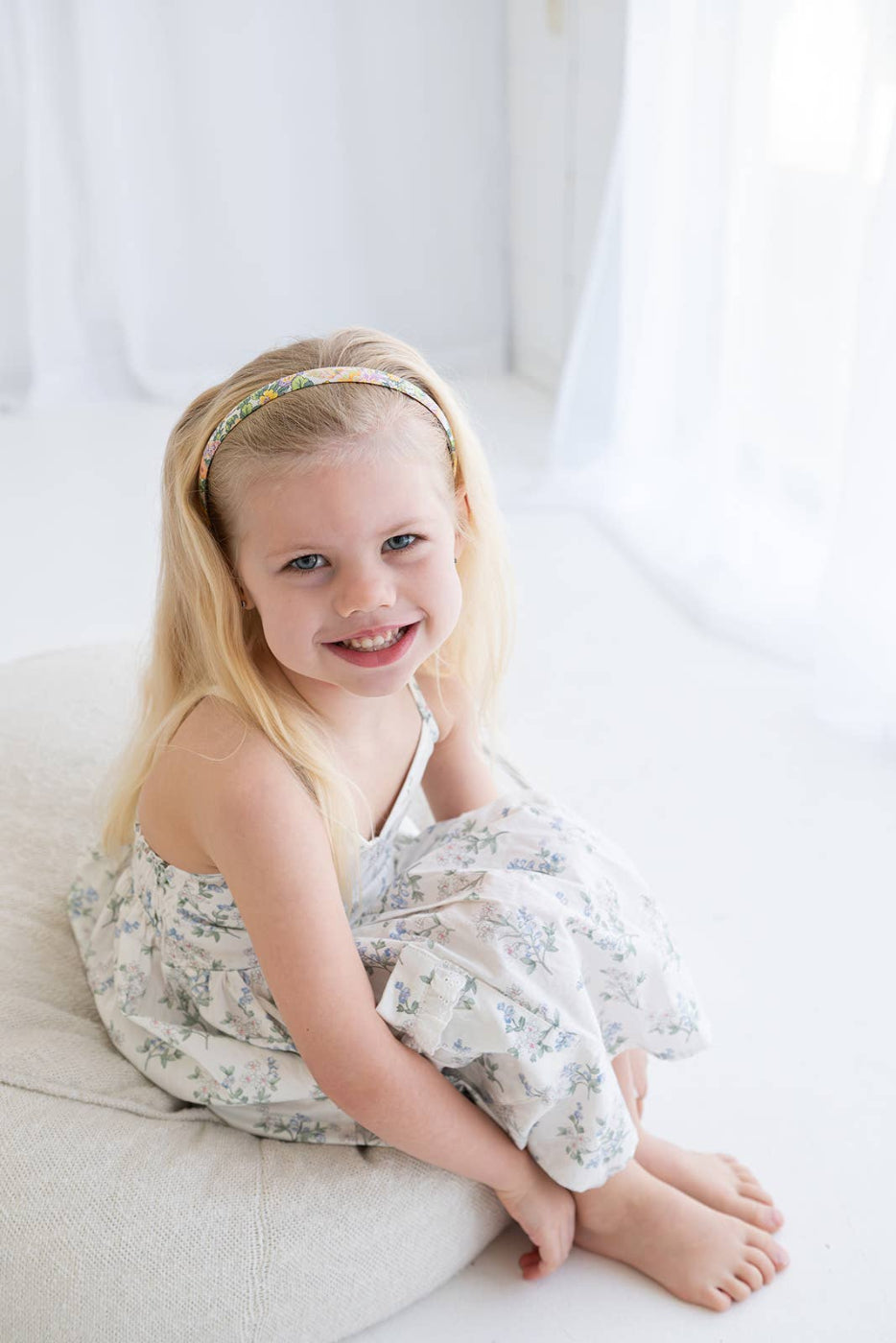 Young girl sitting on a white couch wearing a floral dress and headband