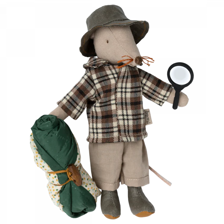 A toy mouse dressed as a wildlife guide, wearing a hat and plaid shirt, holding a magnifying glass and a sleeping bag.