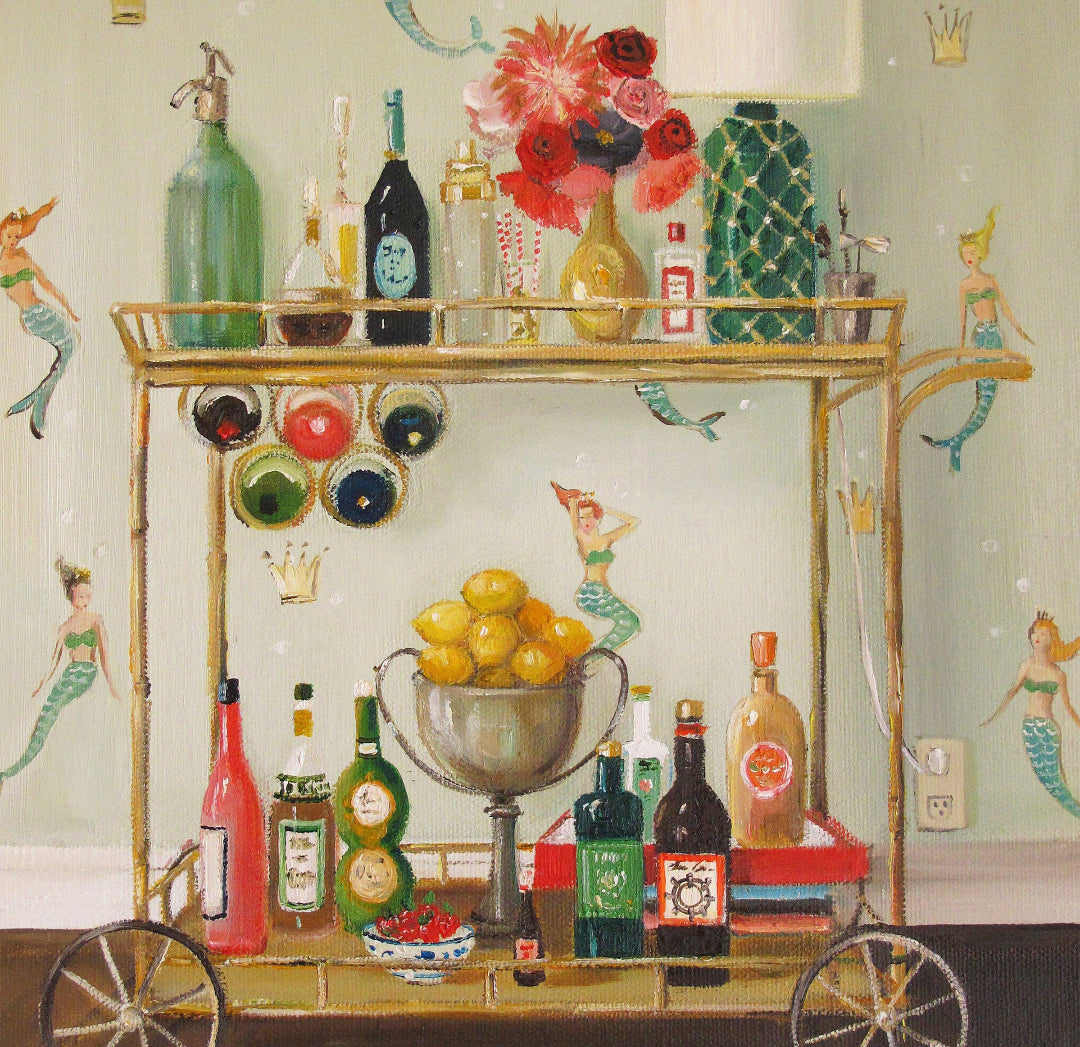 Decorative bar cart with various bottles, fruits, and a lamp against a wall with mermaid decorations.