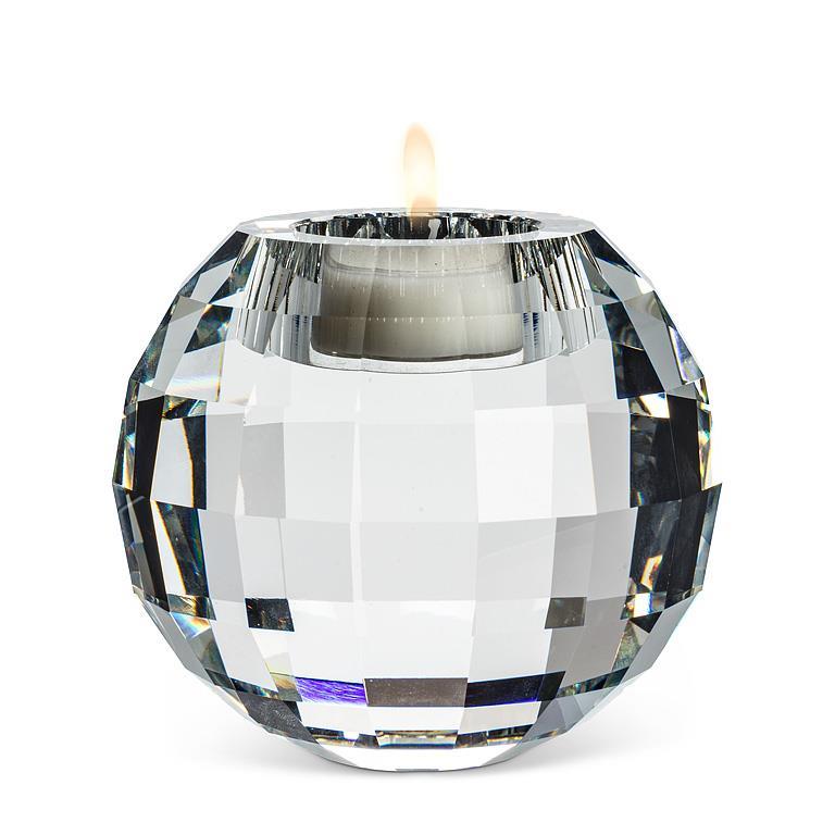 A faceted clear glass candle holder with a lit white tea light candle inside, set against a plain white background.