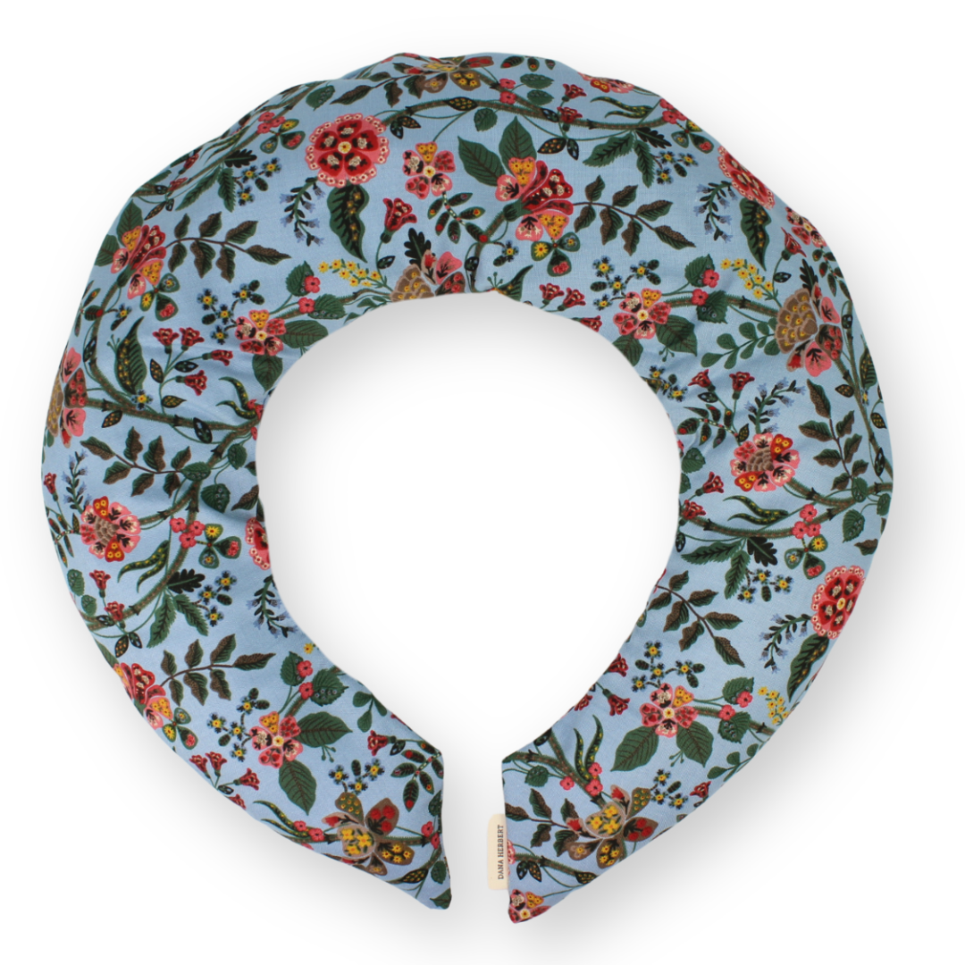 A floral printed neck wrap with a blue background and flowers in orange, red and pink, featuring a removable cotton cover.