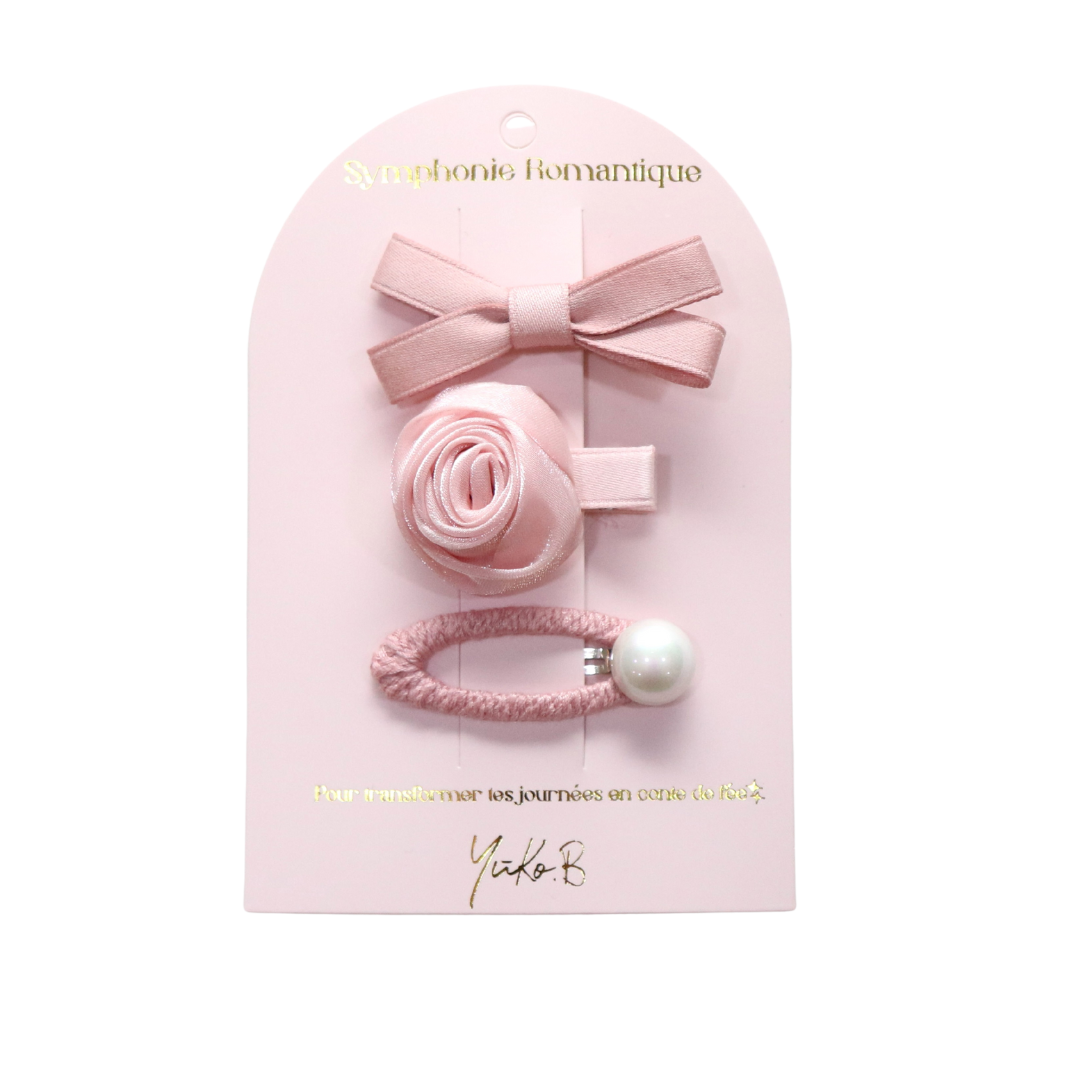 Set of pink hair accessories including a bow, flower, and rubber band on a pink packaging with brand name.
