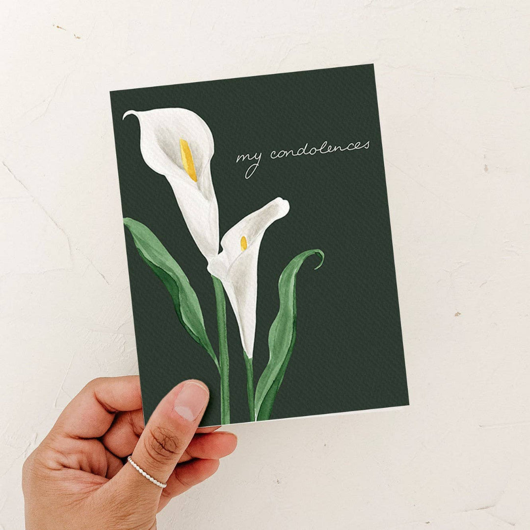 Greeting card with white lilies and 'my condolences' text held by a hand on a light background