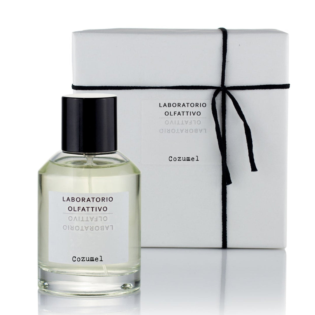 A clear glass bottle of 'Cozumel' eau de parfum with a black cap, next to its white packaging box with a black bow and the brand 'Laboratorio Olfattivo' visible on the label.