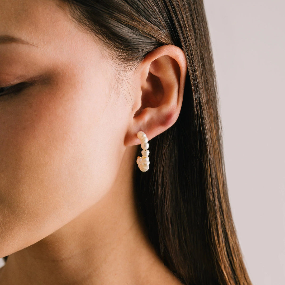 Close-up of a woman wearing pearl hoop earrings with a neutral background