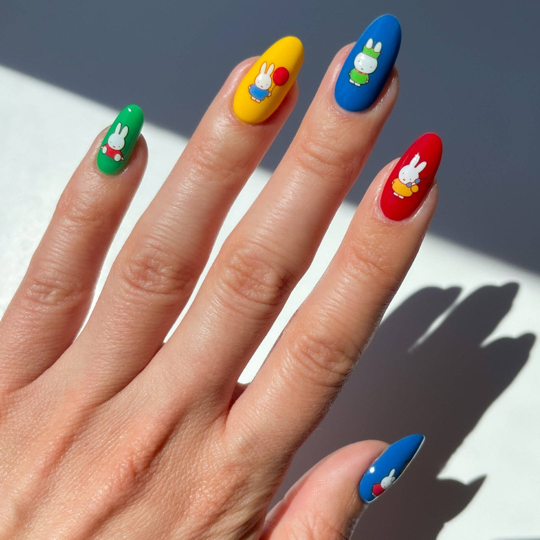 Hand with colorful nail art featuring Miffy characters on a white background
