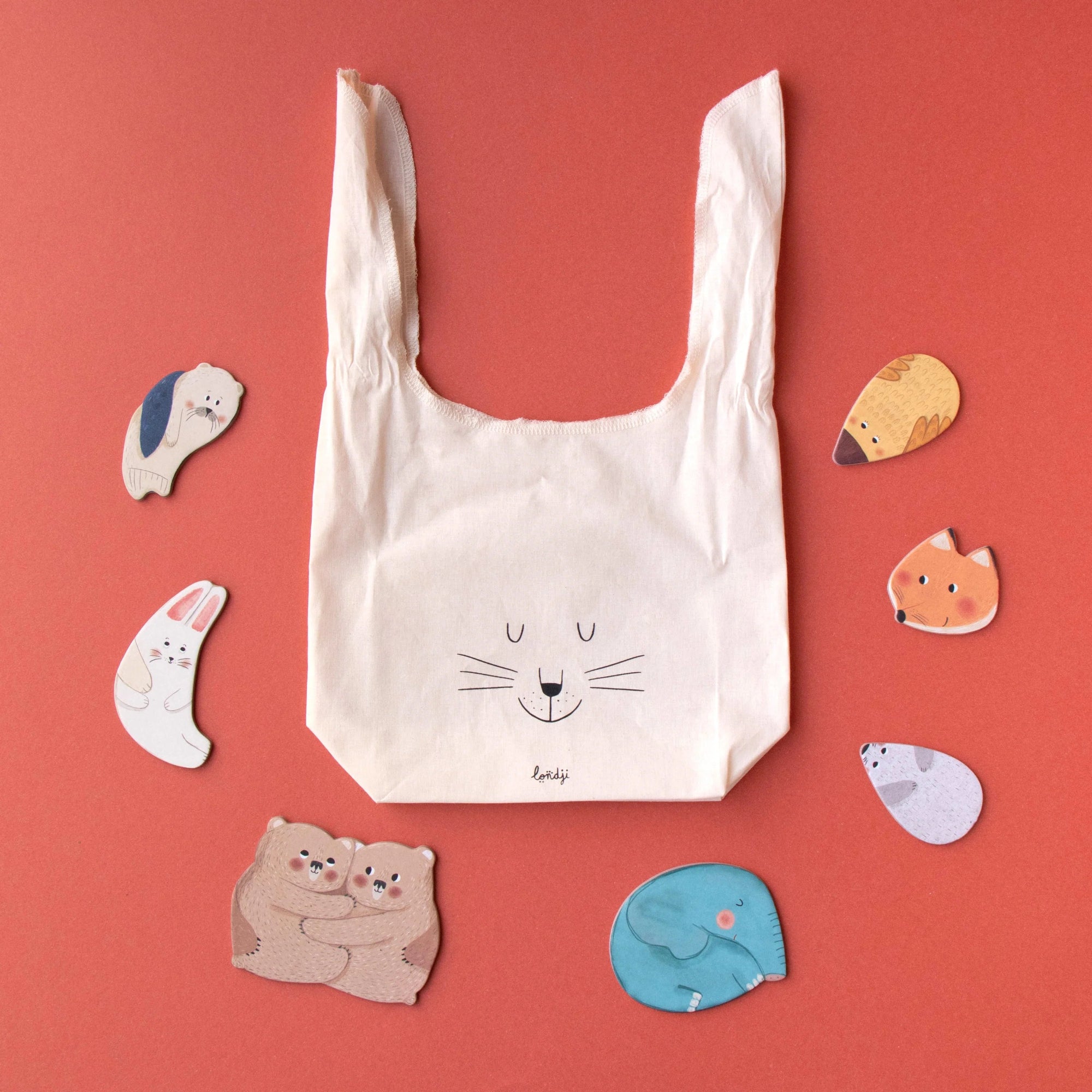 Beige reusable bag with a cat illustration on a red background with animal-shaped objects.