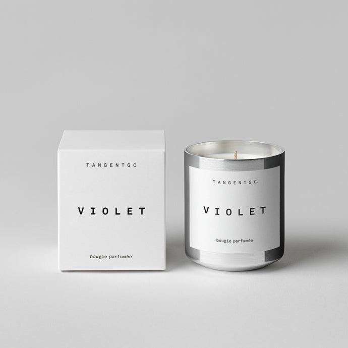 A white scented candle with a label reading 'Tangent Violet', alongside its white box packaging with the same label.