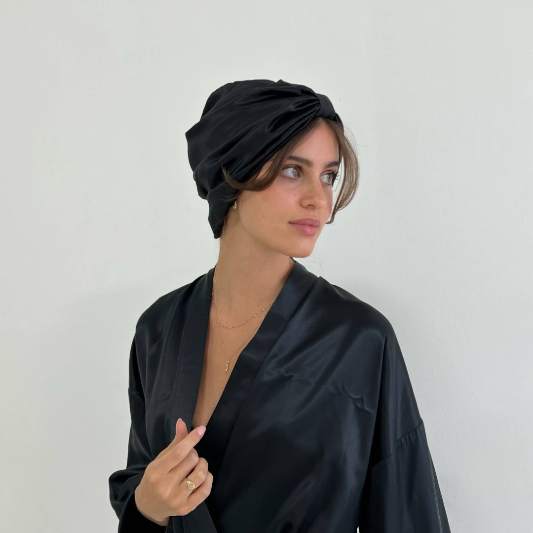 Woman wearing a black headscarf and robe against a plain background