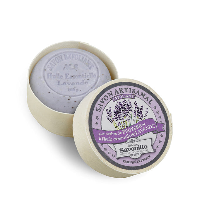 Round lavender-colored exfoliating soap in a wooden box with a label showing the brand and product name.