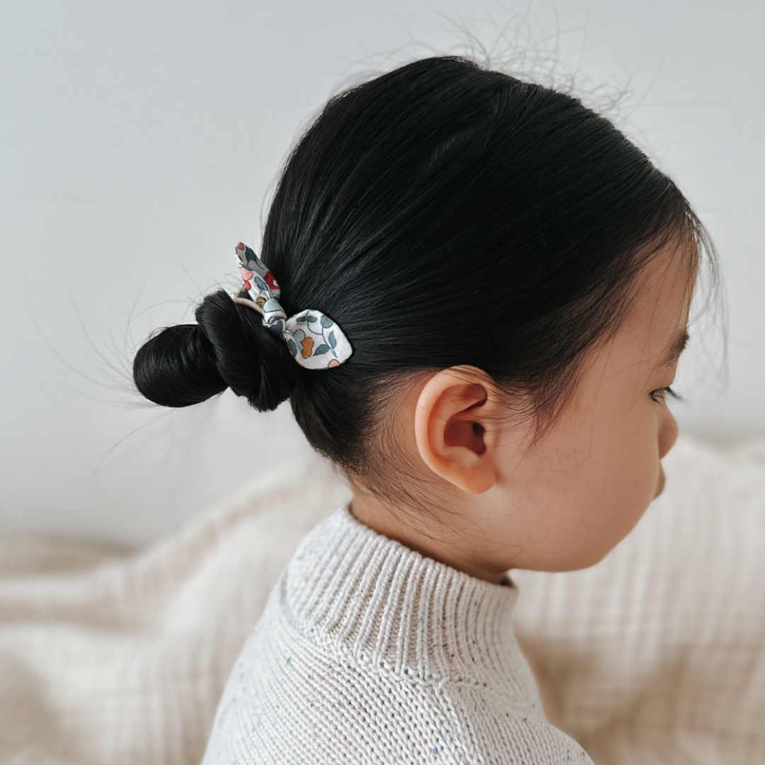 Child with a hair tie in their bun against a neutral background