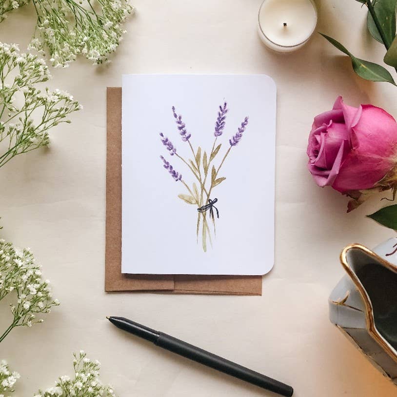 Greeting card with lavender design surrounded by flowers and a candle on a light surface