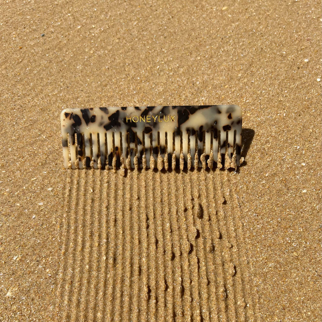 Tortoise comb with 'Honeylux' branding on a sandy surface