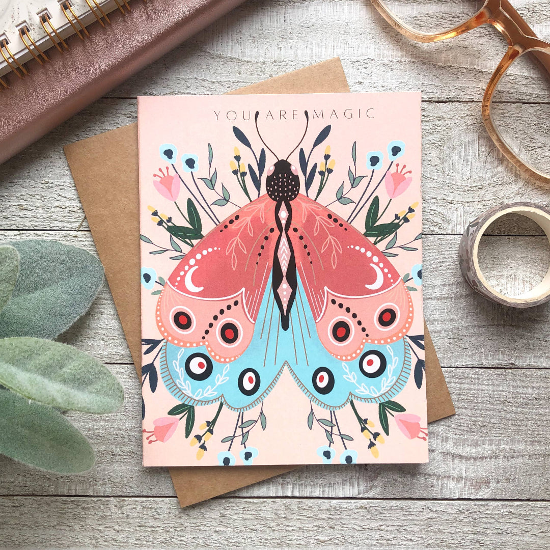Greeting card with butterfly design and 'You Are Magic' text on a wooden surface.