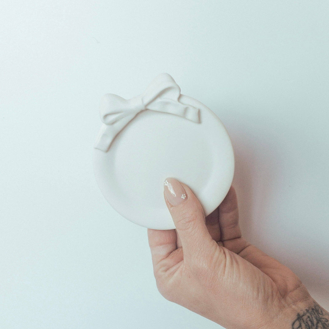 Hand holding a white round dish with a bow on a light background