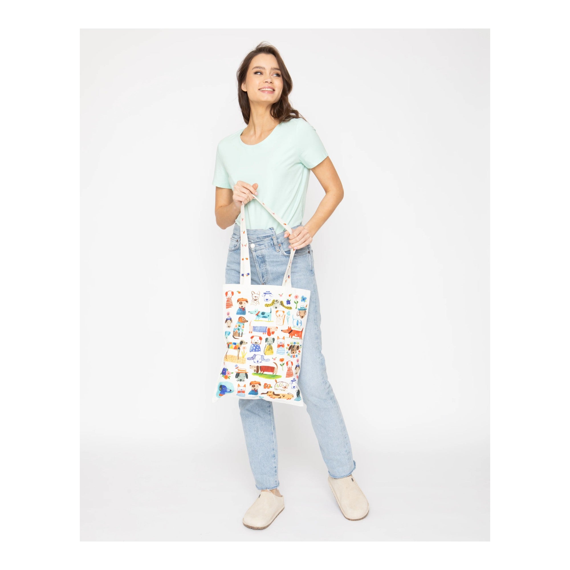 Woman holding a colorful tote bag with various designs on a white background