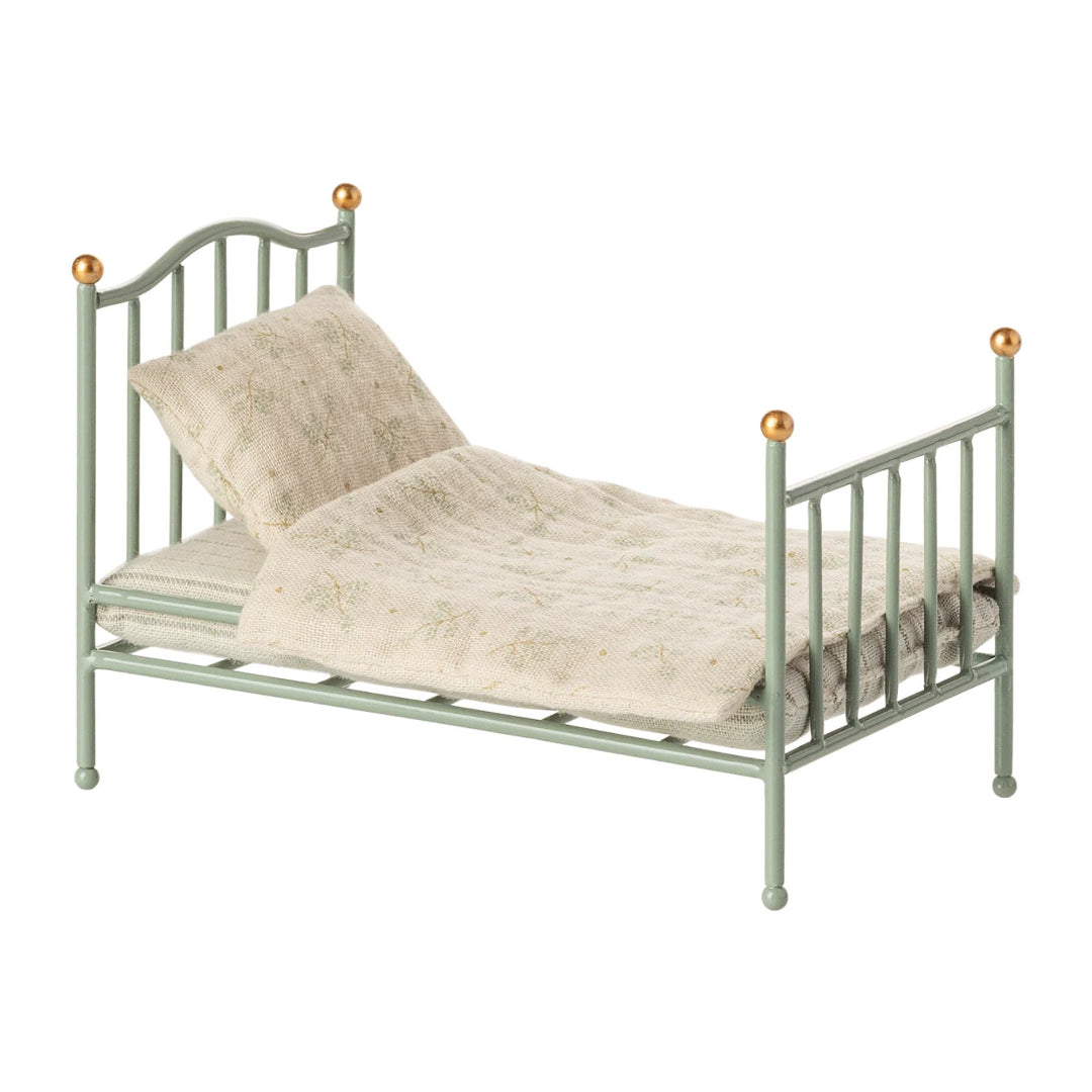 Small mint metal bed with floral bedding on a white background
