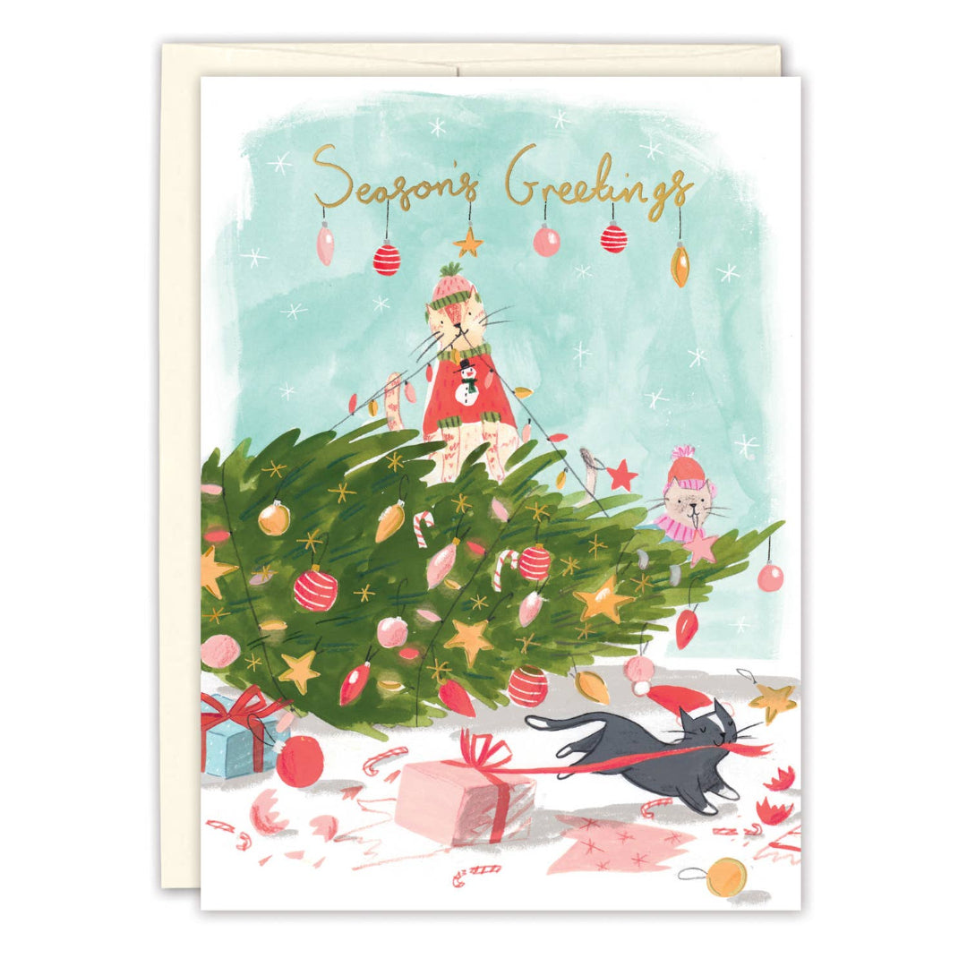 A Christmas greeting card with a watercolor illustration of a woman decorating a Christmas tree, a cat wearing a Santa hat, wrapped gifts, candy canes, and the words 'Season's Greetings' at the top. The card is shown with a cream envelope behind it on a white background.