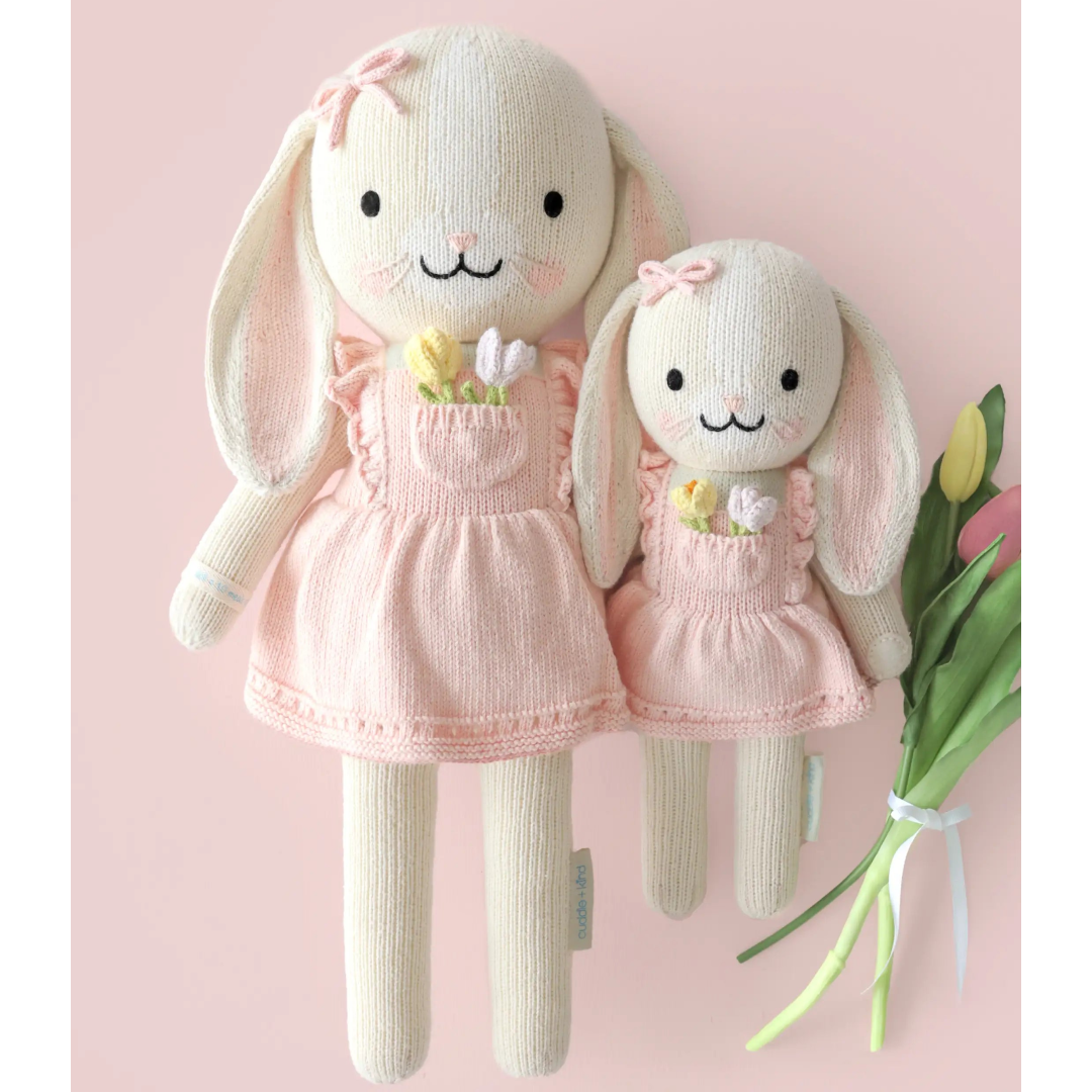 Two knitted bunny dolls in pink dresses on a light pink background with tulips.