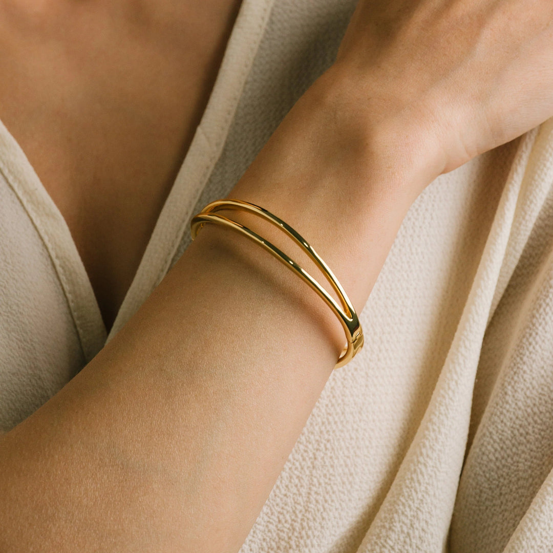 Gold bracelet on a wrist with a neutral background