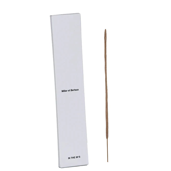 A single incense stick standing vertically next to its tall white rectangular box, which has the text 'Miller et Bertaux' and 'IN THE 80'S' printed on it, set against a white background.