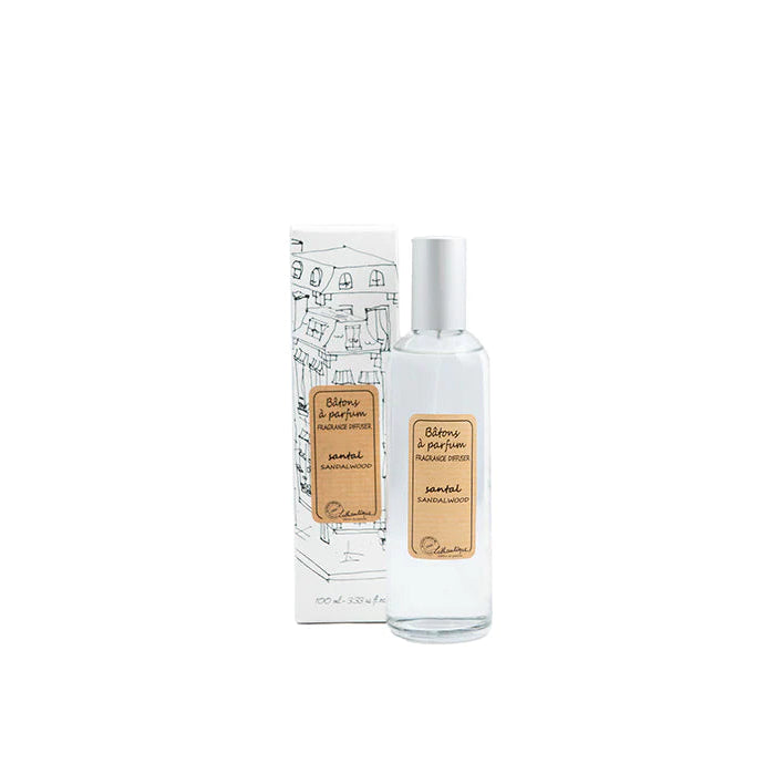 A clear glass room spray bottle with a label next to its packaging featuring a drawing of a house.