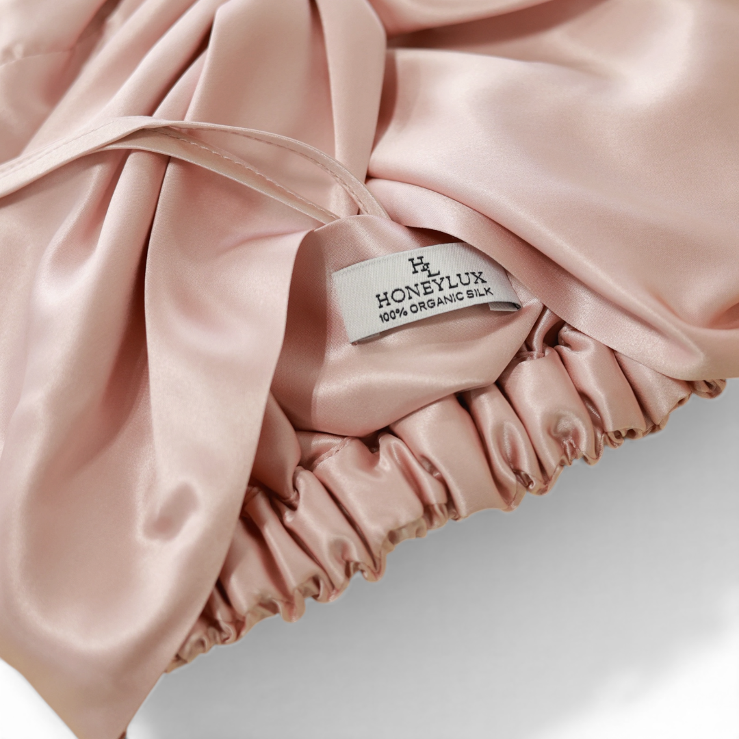 Pink silk hair bonnet with 'HONEYLUX' 100% Oraganic Silk label on a light background