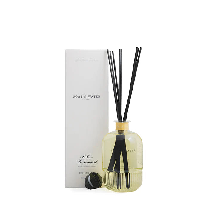 Reed diffuser with black sticks in a clear bottle next to a white box labeled 'Soap & Water'.