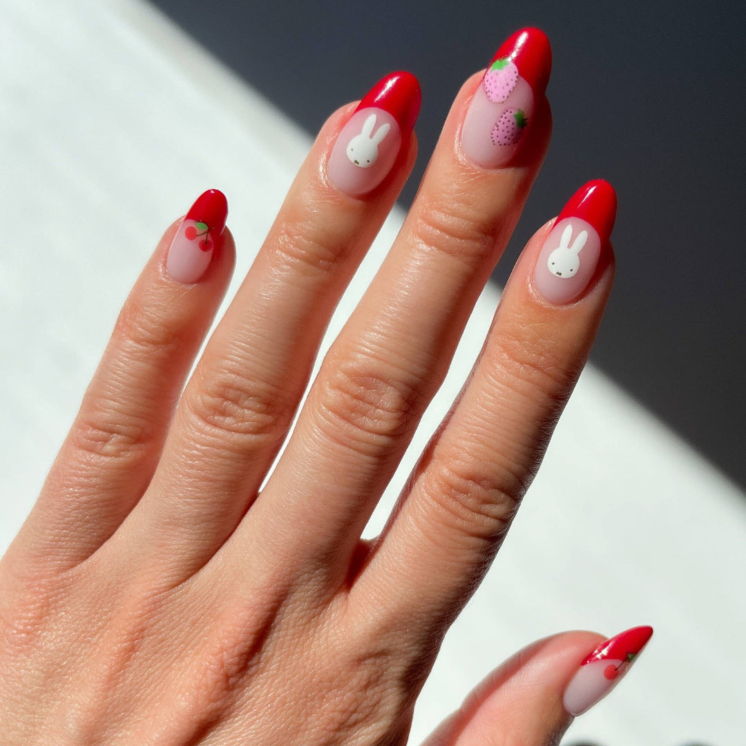 Close-up of nails with red tips and Miffy nail stickers on a neutral background