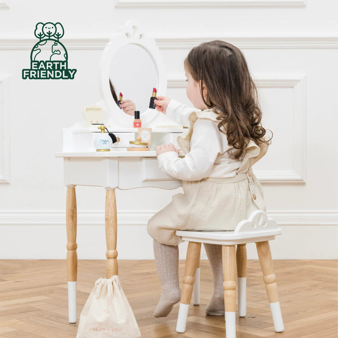 Child playing with pretend makeup at a vanity table in a room with 'Earth Friendly' logo.