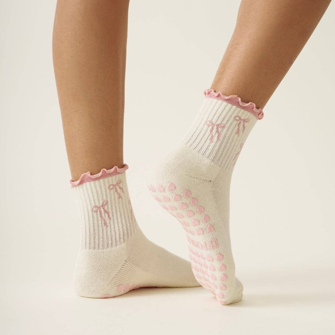 White socks with pink bows and ruffles worn by a person on a light background