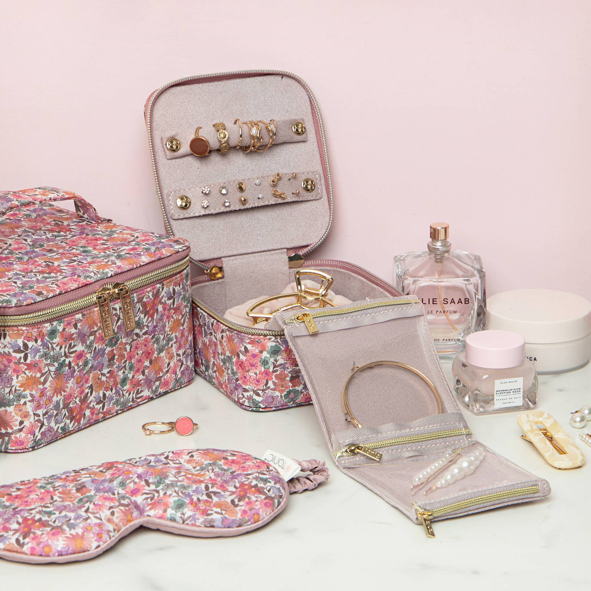 Jewelry case with floral design, jewelry, and perfume on a light pink background