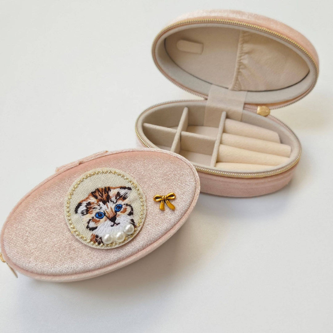 Pink jewelry case with embroidered cat design on a white background