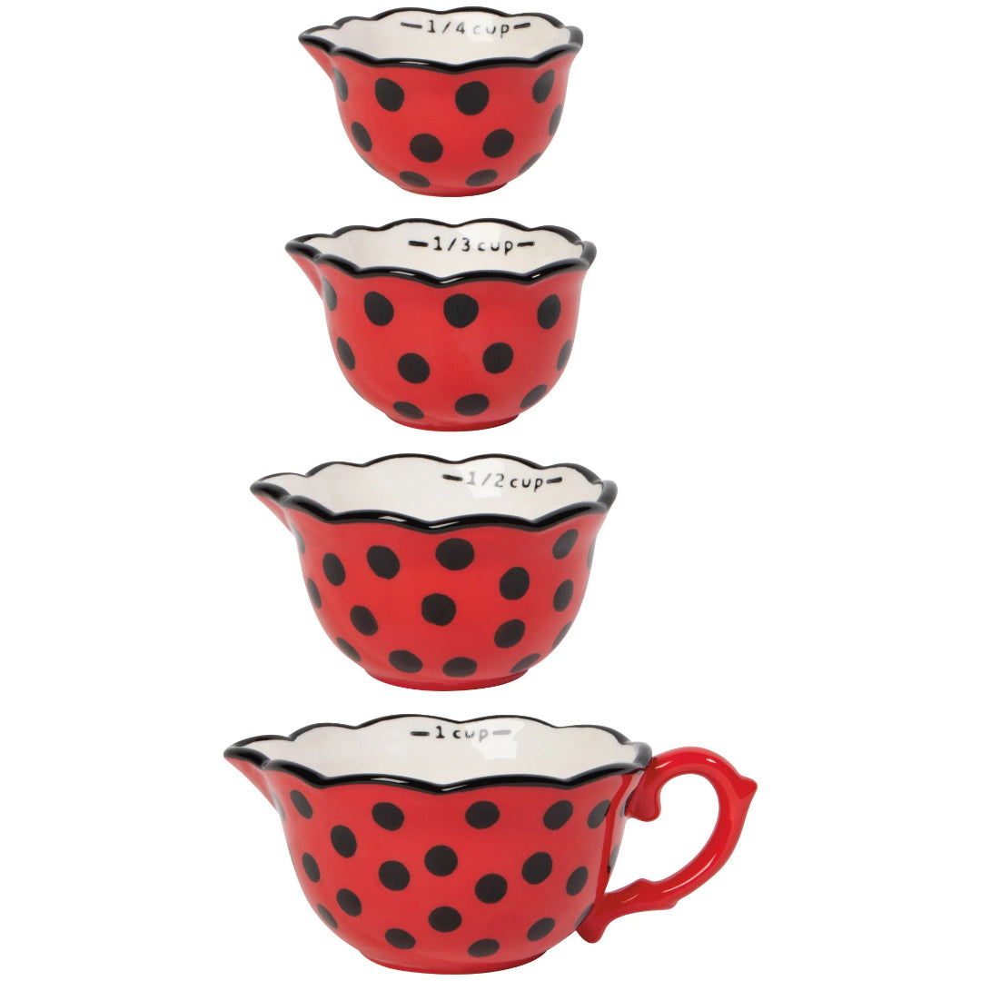Set of four red measuring cups with black polka dots on a white background