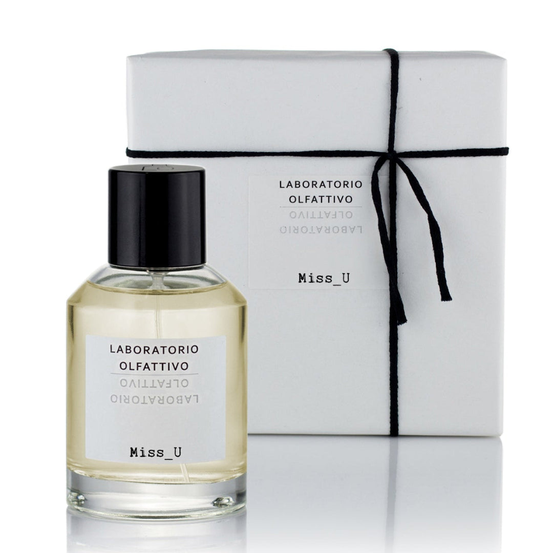A glass bottle of 'Miss_U' eau de parfum with a black cap, in front of a white box with the product name and a subtle logo.