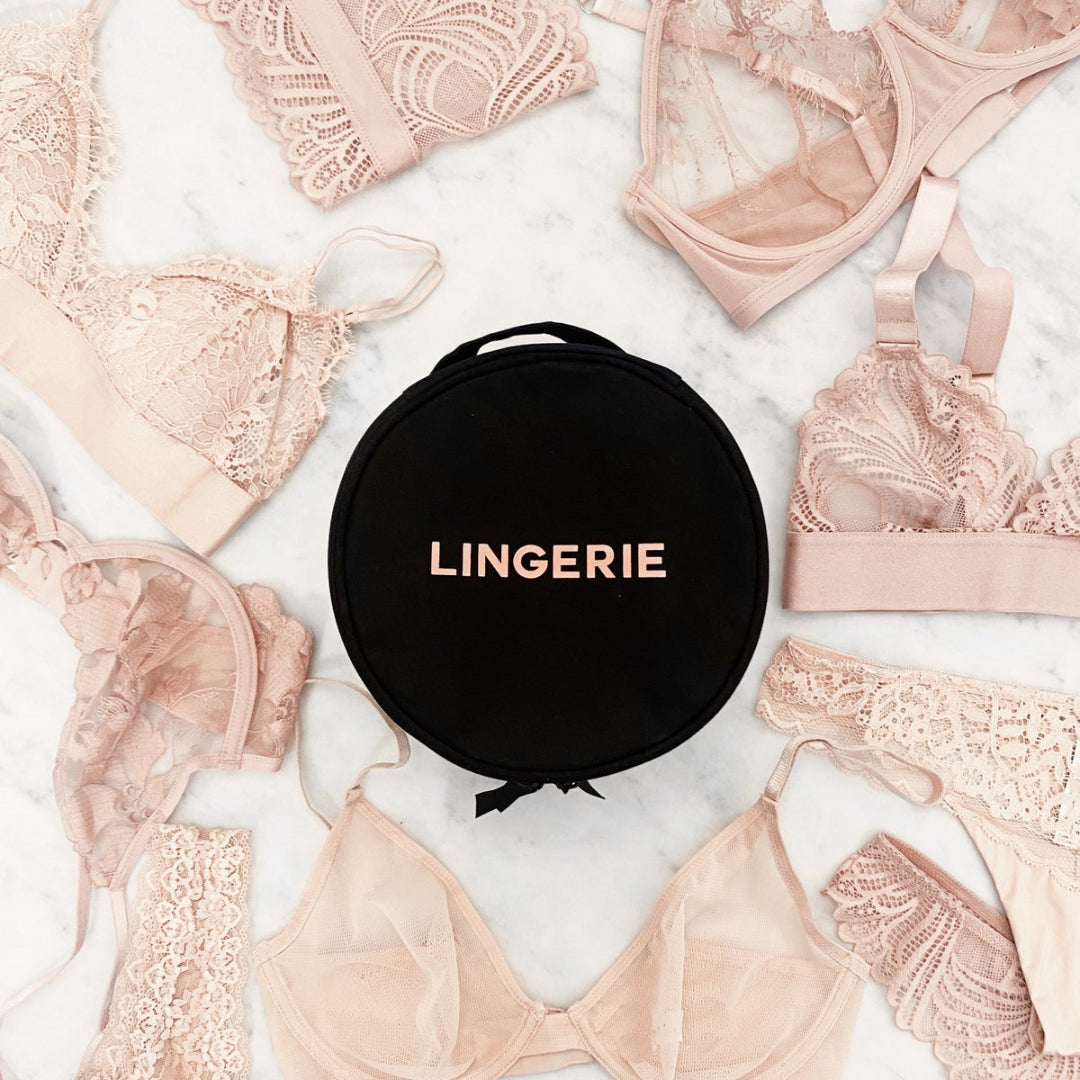 A collection of beige and pink lingerie pieces displayed around a round black lingerie case with a grosgrain ribbon closure.