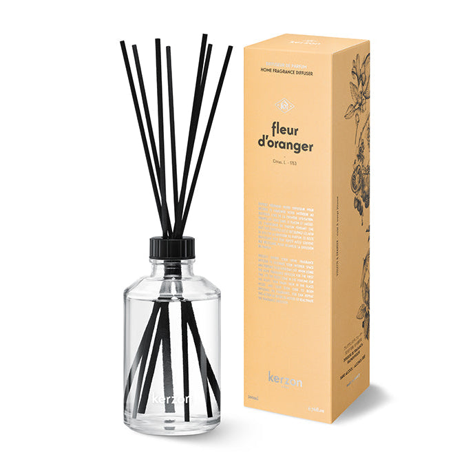 A clear glass fragrance diffuser with black sticks inside, alongside a yellow packaging box with the product name 'Fleur d'Oranger' and an image of orange blossoms.